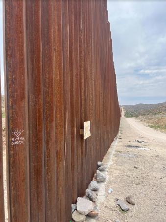 A close-up view of the gated border wall between U.S. and Mexico. One of the gate poles has a small drawing of a heart and the words 